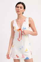 Model wearing white satin mini dress with colorful pattern and red sandals