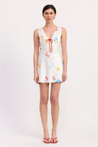 Model wearing white satin mini dress with colorful pattern and red sandals
