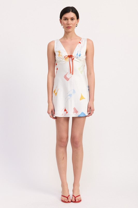 Model wearing white satin mini dress with colorful pattern and red sandals