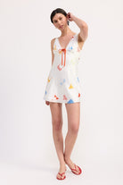 Model wearing white satin mini dress with colorful pattern and red sandals
