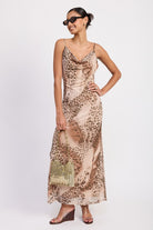 Woman in flowing leopard print maxi dress with soft cowl neckline, holding gold bag