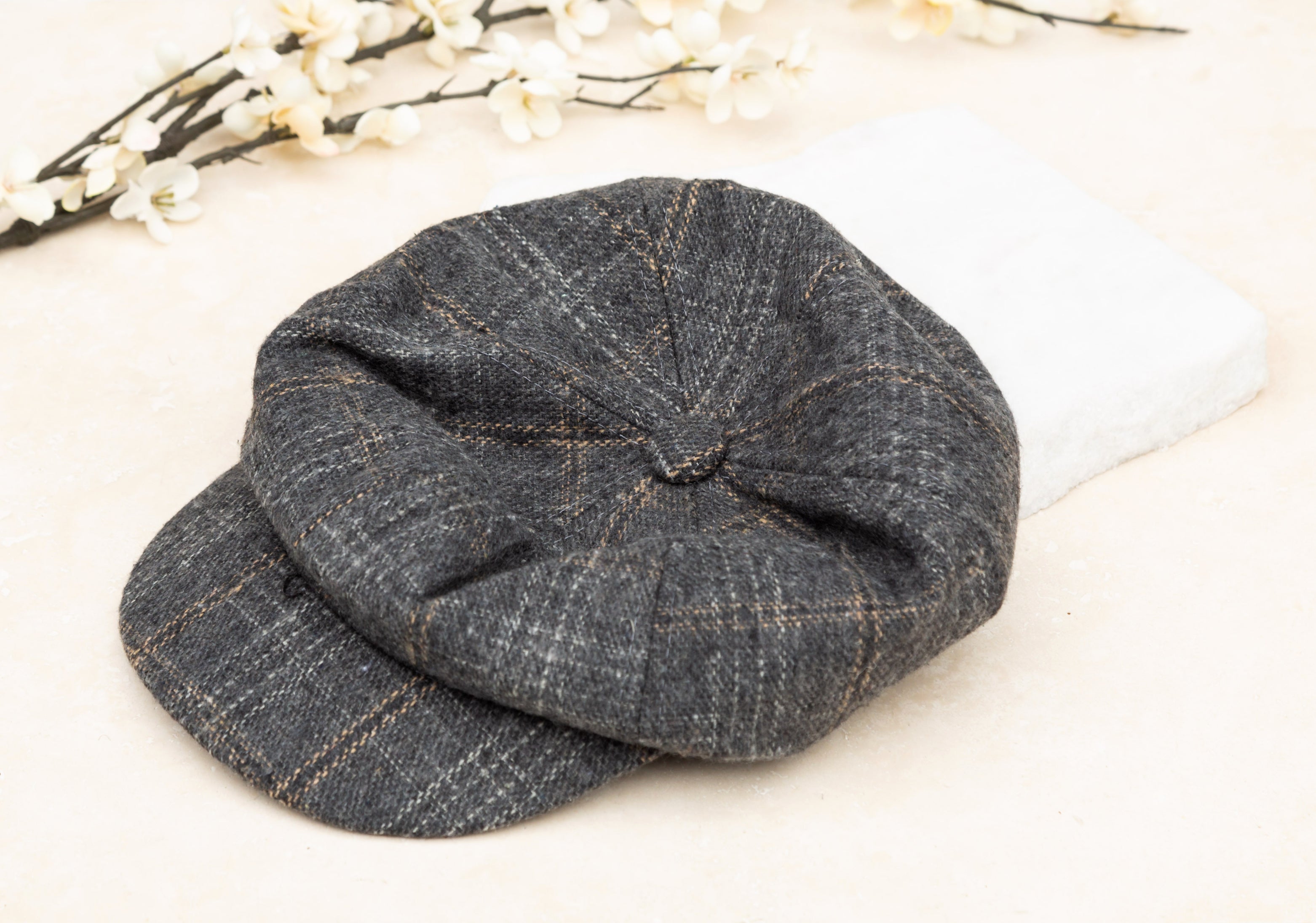 A gray tweed baker boy cap with a structured brim, flat lay on white background