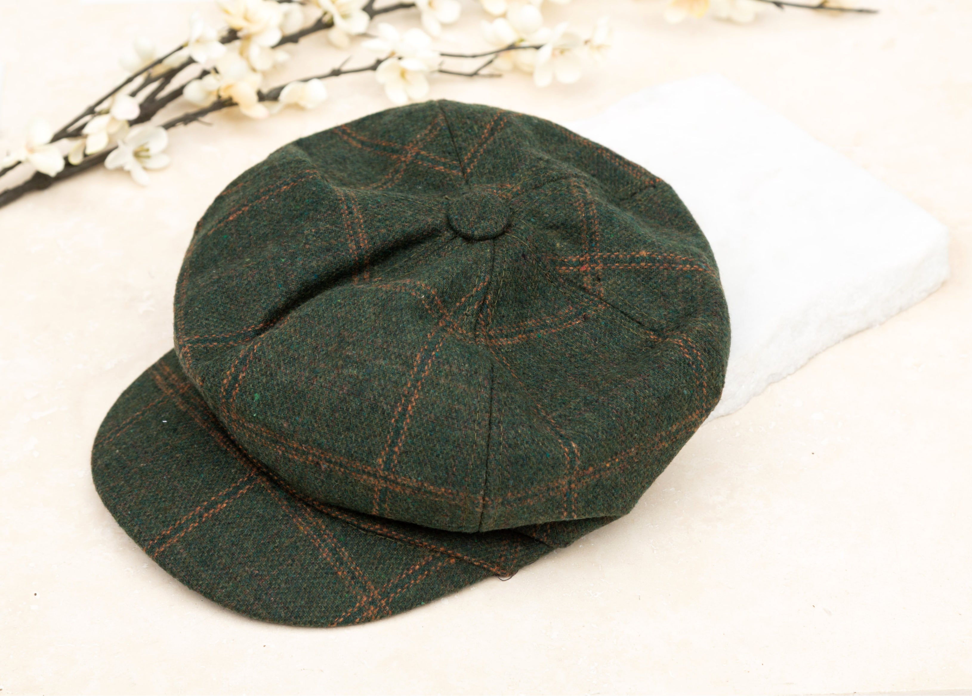 A hunter green tweed baker boy cap with a structured brim, flat lay on white background
