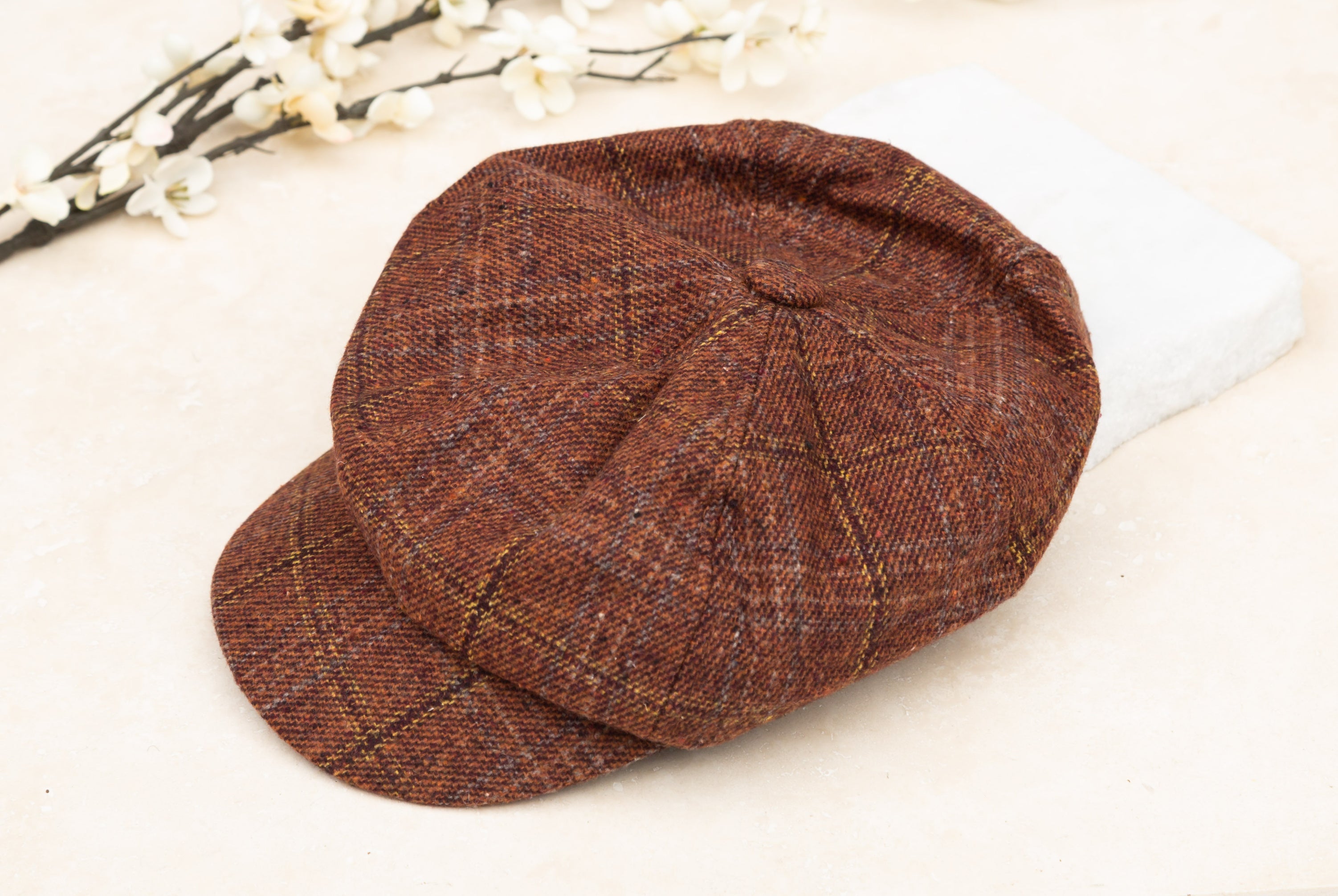 A rust tweed baker boy cap with a structured brim, flat lay on white background