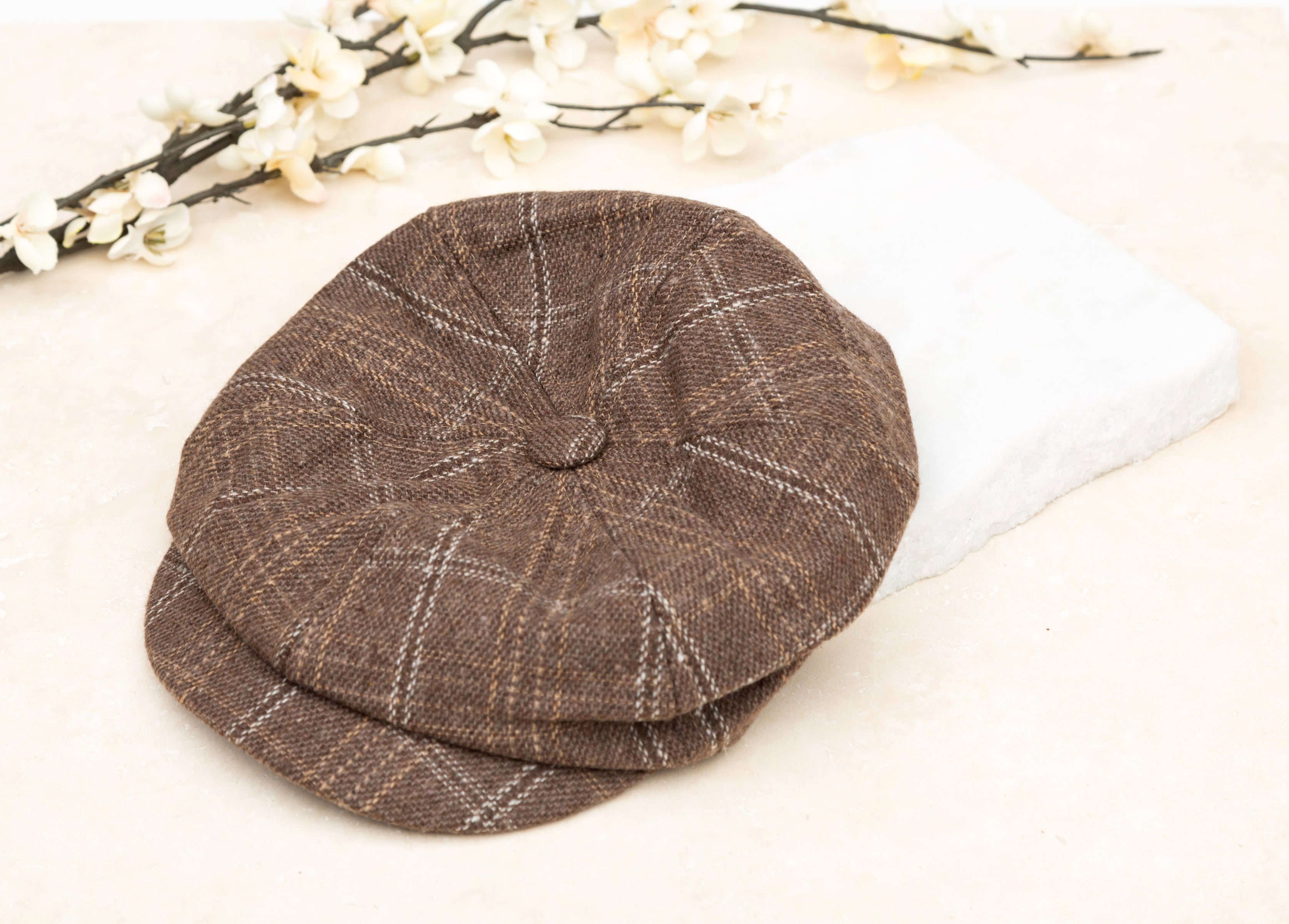 A tan tweed baker boy cap with a structured brim, flat lay on white background