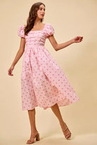 Model wearing a pink polka dot midi dress with puff sleeves, pleated bodice, and flowing skirt | AVAH Collections
