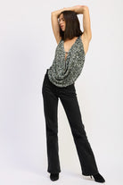 Full-body view of model posing with arms raised, wearing the silver draped sequin halter top and black jeans.