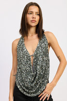 Model wearing a silver sequin draped halter top with a deep plunging neckline, paired with black pants.