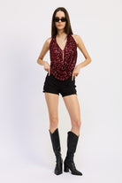 Full-body view of model in red sequin halter top, black shorts, and tall black boots.