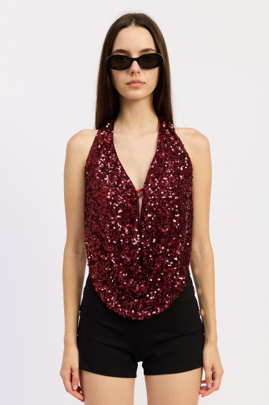 Model wearing a red sequin draped halter top with deep neckline, paired with black shorts and sunglasses.