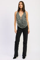Model standing straight in a silver draped sequin halter top paired with black jeans and black boots.