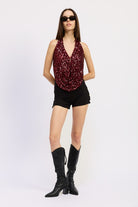 Full-body view of model in red sequin halter top, black shorts, and tall black boots.