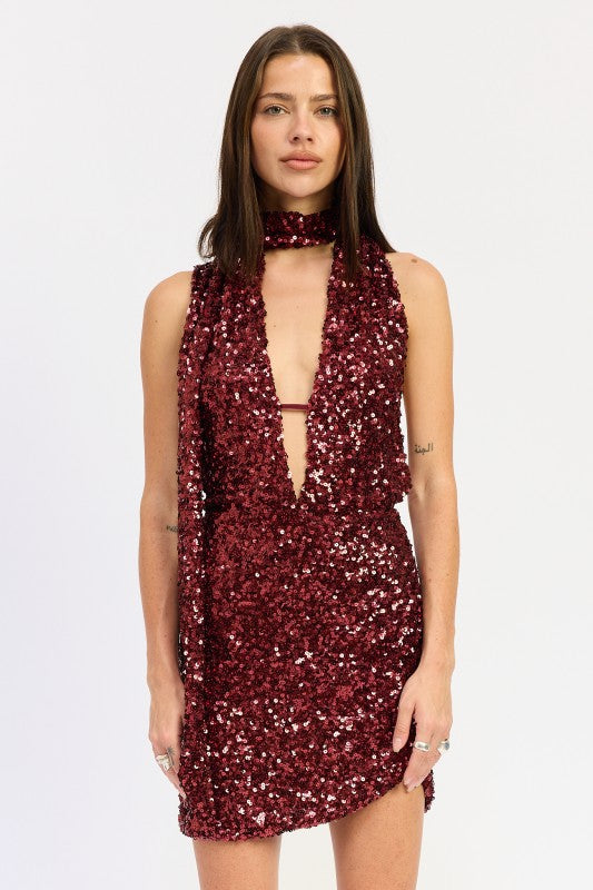 Front view of model wearing a wine sequin deep-plunge mini dress with draped scarf detail.
