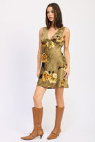 Full-body side view of model in olive floral tie-front mini dress with tall tan boots