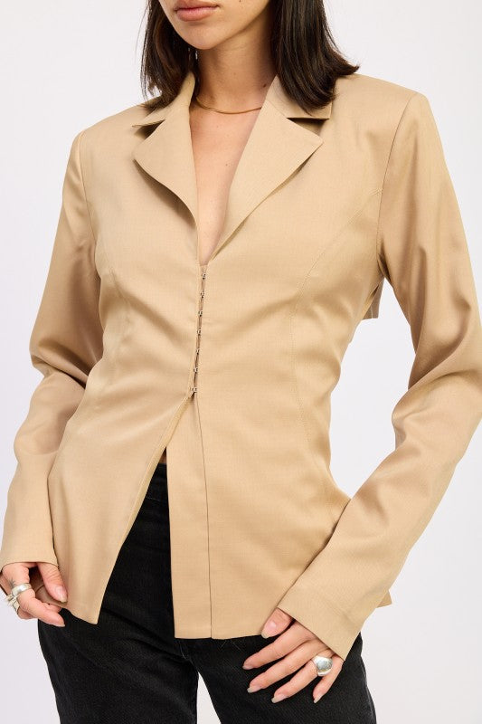 Close-up of neutral camel fitted blazer with hook-and-eye closure and front slit detail.