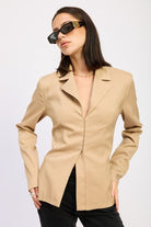 Model in neutral fitted blazer with notched lapel and sculpted waist, styled with sunglasses – front view.