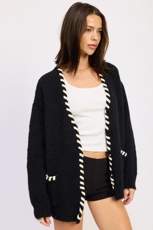 Model posing in black cardigan with white contrast edge — angled front view.
