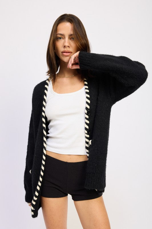 Model wearing a black cardigan with white trim, white top, and black shorts on a light gray background
