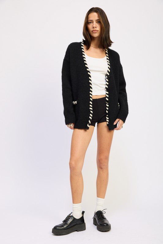 Full outfit view of contrast-trim cardigan sweater styled with black shorts and loafers.