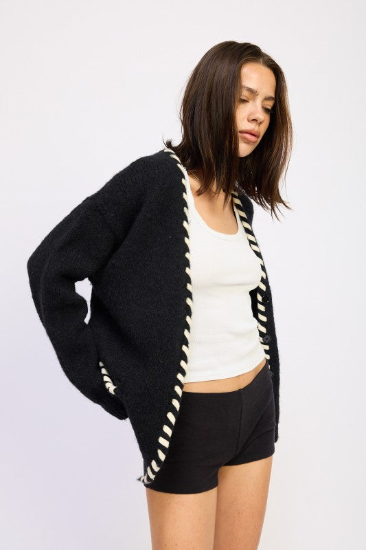 Model wearing a black cardigan with white leather trim on a plain background
