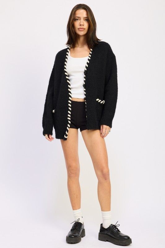 Full outfit view of contrast-trim cardigan sweater styled with black shorts and loafers.