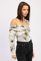 Model posing in AVAH off-shoulder ruched mesh bodysuit with long sleeves and fitted floral print.