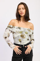 Model front view wearing AVAH olive floral off-shoulder ruched mesh bodysuit with sheer long sleeves styled with black denim.