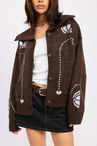 Model in chocolate brown collared cardigan with floral knit details, layered over white tank and paired with mini skirt.