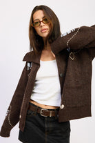 Model in chocolate brown collared cardigan with floral knit details, layered over white tank and paired with mini skirt