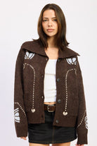 Woman wearing chocolate brown collared cardigan with floral intarsia knit, styled with white tank and black mini skirt-AVAH