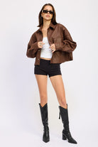 Model styled in AVAH cropped jacket with grid embossing, paired with black shorts, white tank, and tall black boots.