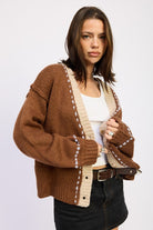 Side angle of brown knit cardigan with beige trim and relaxed sleeves.
