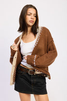 Model wearing brown contrast-trim knit cardigan with cream accents and white tank top.
