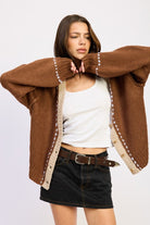 Model wearing brown contrast-trim knit cardigan with cream accents and white tank top.
