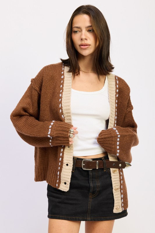 Model wearing brown contrast-trim knit cardigan with cream accents and white tank top.
