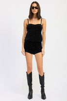 Model wearing black velvet rhinestone cami top and matching shorts styled with tall black boots.