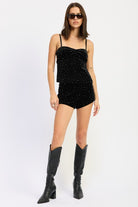 Model wearing black velvet rhinestone cami top and matching shorts styled with tall black boots.