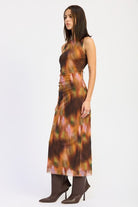 Side view of model in rust sleeveless maxi dress showing figure-hugging shape and back slit detail.
