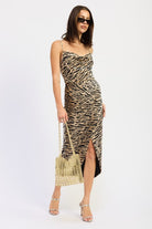 Model in zebra print cowl neck midi dress holding a gold woven bag, paired with silver heels and black sunglasses-AVAH