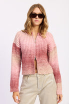 Model wearing blush ombre ribbed zip-up cardigan sweater with light trousers.
