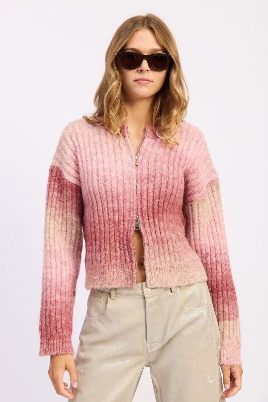 Model wearing blush ombre ribbed zip-up cardigan sweater with light trousers.
