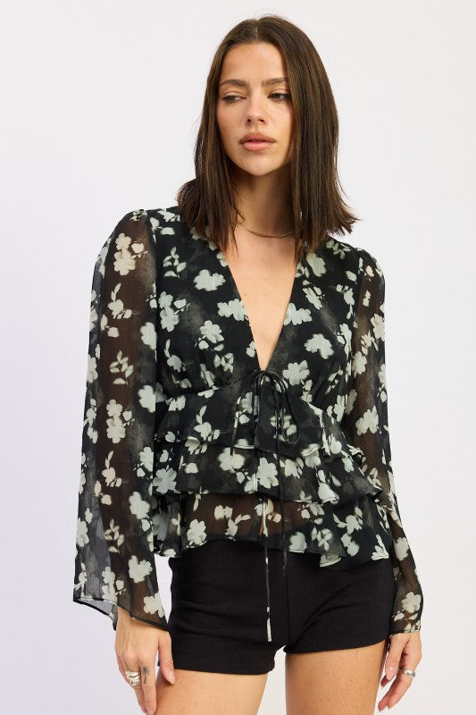 Front view of model wearing black sheer floral peplum blouse with V-neckline.
