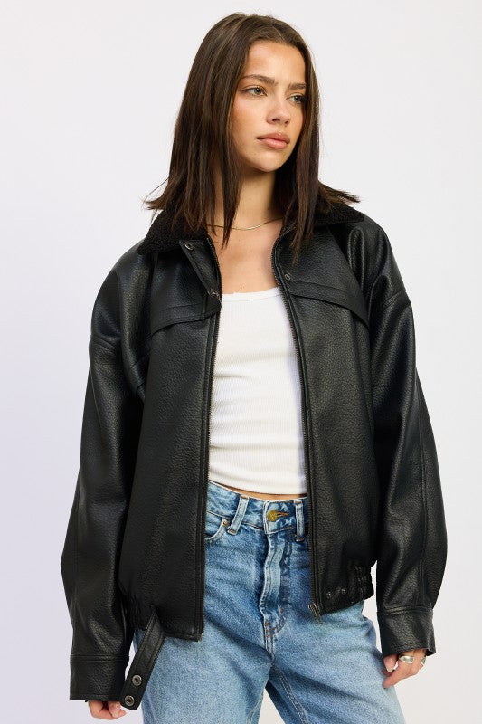 Model wearing black vegan leather bomber jacket with sherpa collar, styled with white tank and light wash jeans.