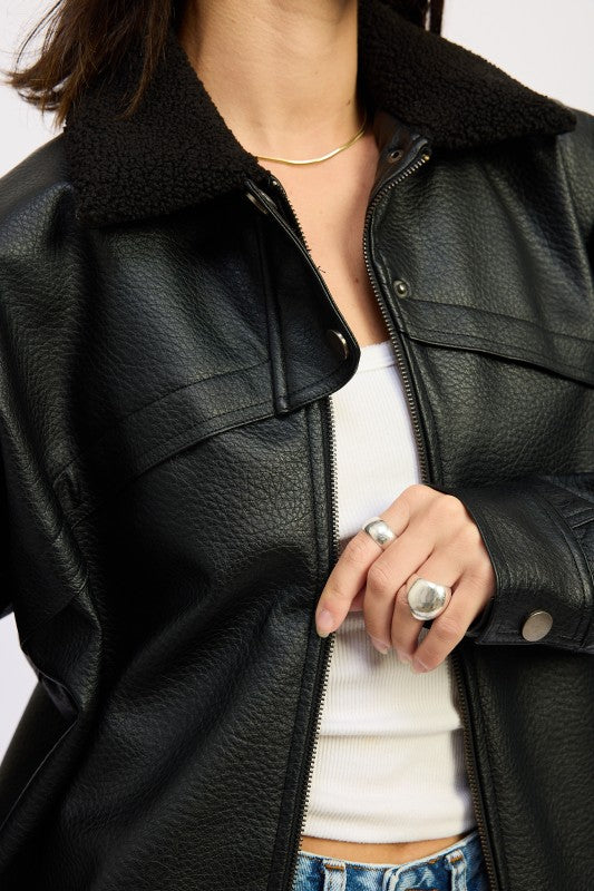Close-up of black vegan leather bomber jacket showing sherpa collar and front zipper detail.

