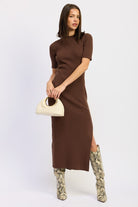Model posing in mocha midi dress and snake skin high boots holding a cream handbag.
