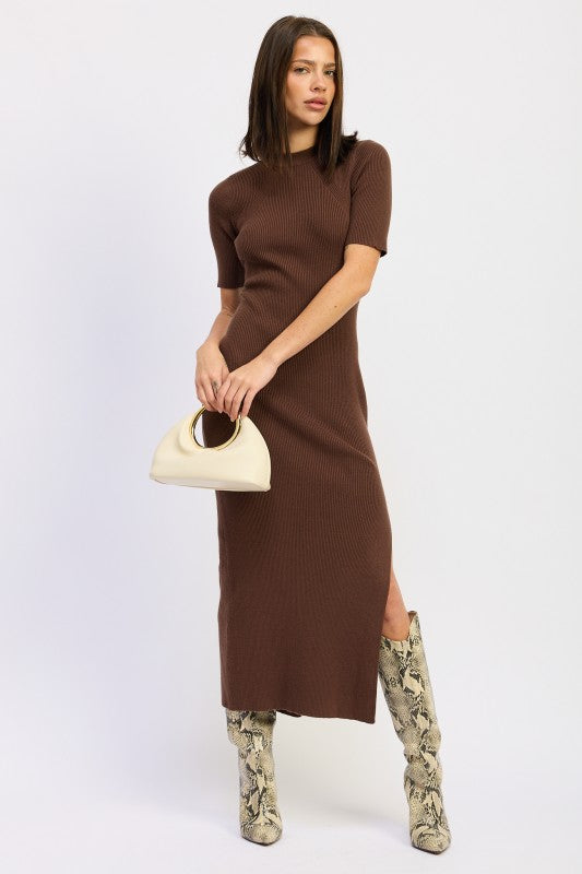 Model posing in mocha midi dress and snake skin high boots holding a cream handbag.
