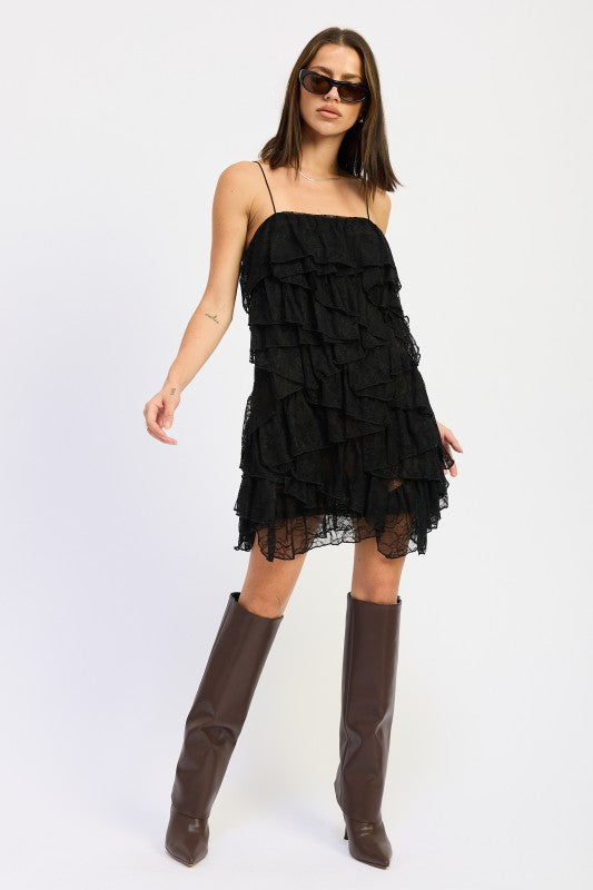 Model wearing a black tiered lace dress and brown knee-high boots on a white background