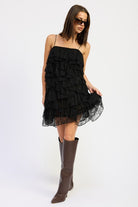 Side pose showing movement and texture of black ruffle lace mini dress.
