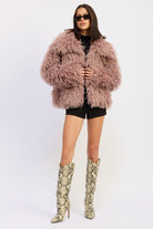 Model wearing the mauve textured coat pulled close at the front with high boots and black shorts.