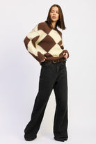 Model styled in cozy argyle pullover sweater with bold diamond design, worn with relaxed black trousers for chic off-duty style.